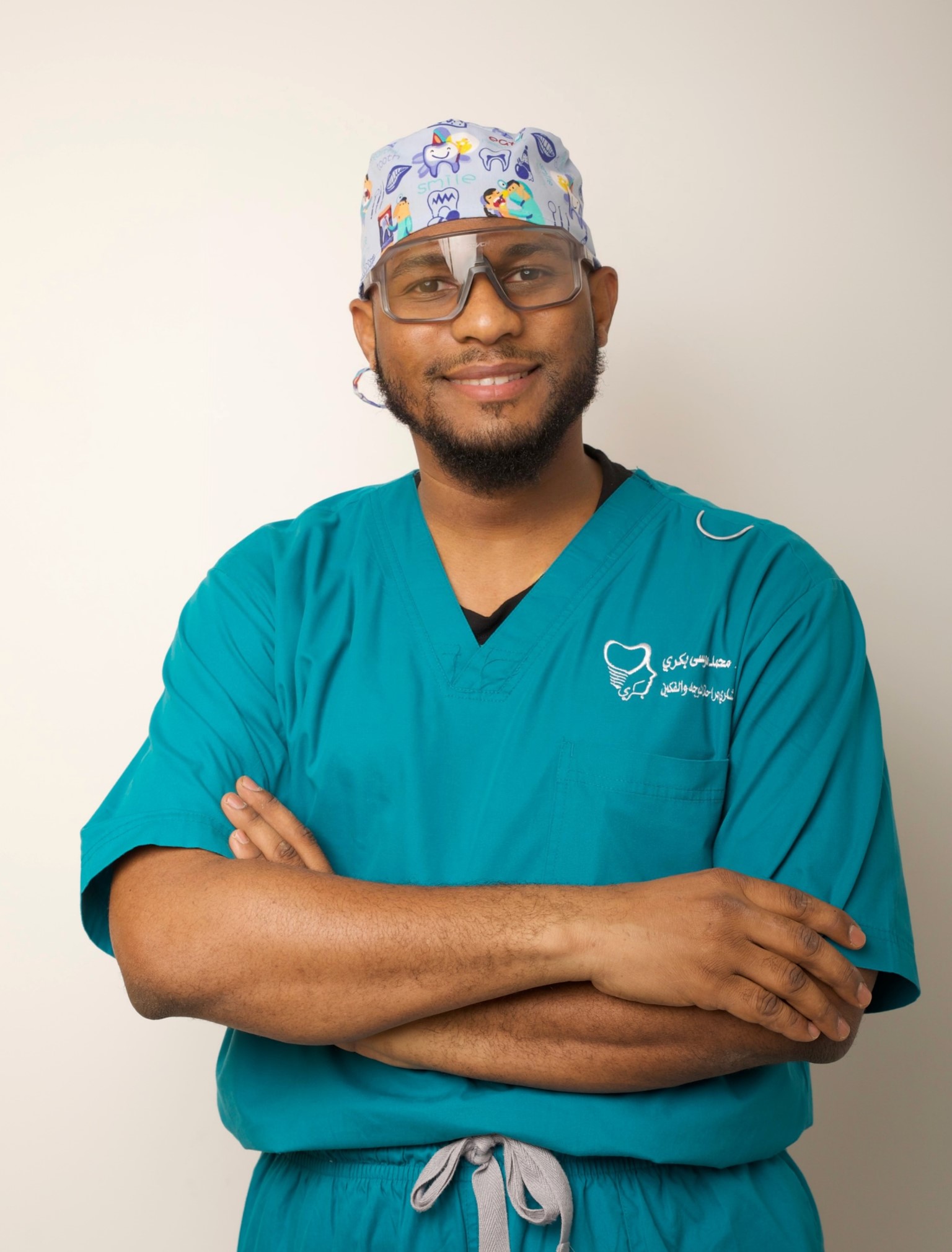 Dr. Mohammed Bakri in teal surgical scrubs and a patterned surgical cap, arms crossed and smiling