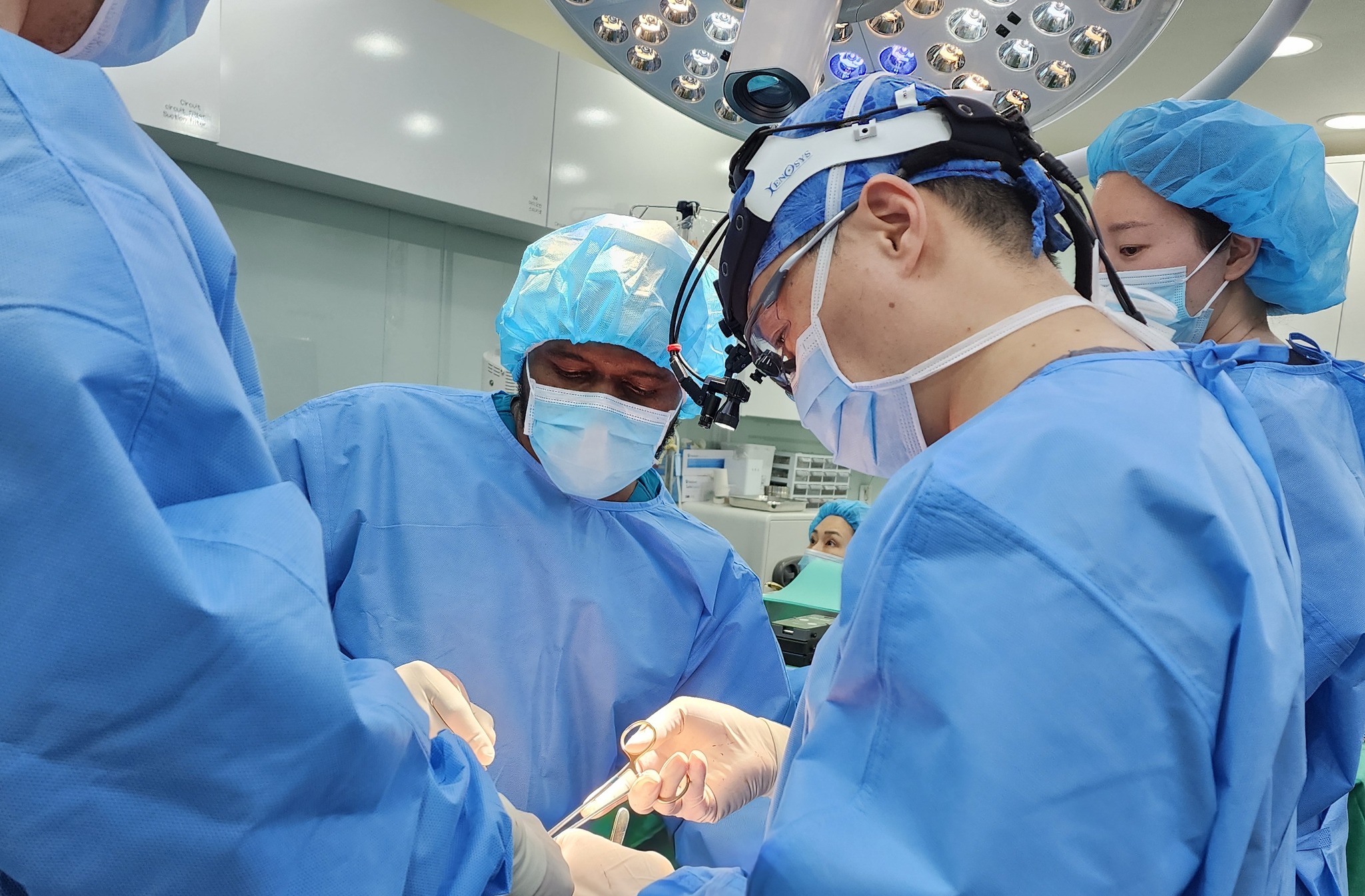 Dr. Bakri operating with a surgical team under theatre lights, surgeon wearing a headlight and loupes